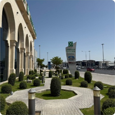 Exterior view of a modern, multi-story building with unique architectural features, set amidst green landscaping and a clear sky.