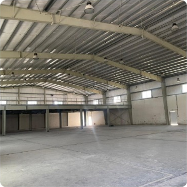 Interior view of a large, empty industrial warehouse with high ceilings and metal support beams.